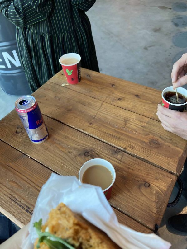 Ein quadratischer Holztisch mit Kaffee in Pappbechern und einem Red Bull